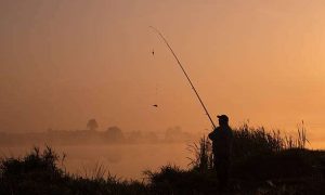 Silhouette of angler with fishing rod at sunrise.