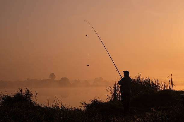 Silhouette of angler with fishing rod at sunrise.
