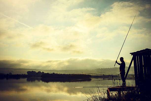 Fisherman holding fishing rod on wooden pier with misty lake.