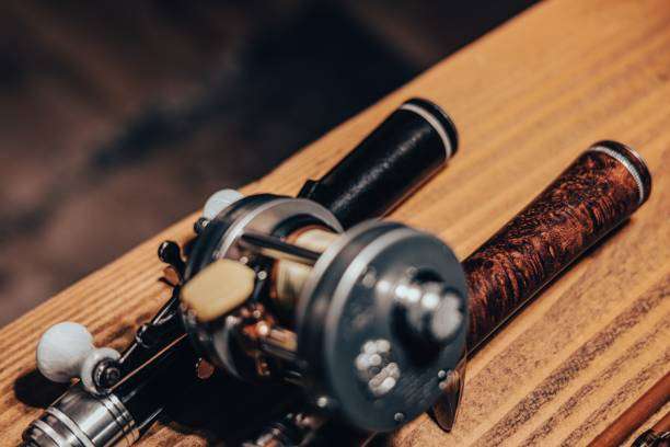Close up of a classic fishing rod reel on a wooden surface.