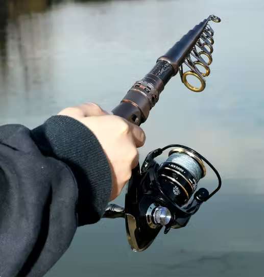 Hand holding a compact telescopic fishing rod and reel over water.