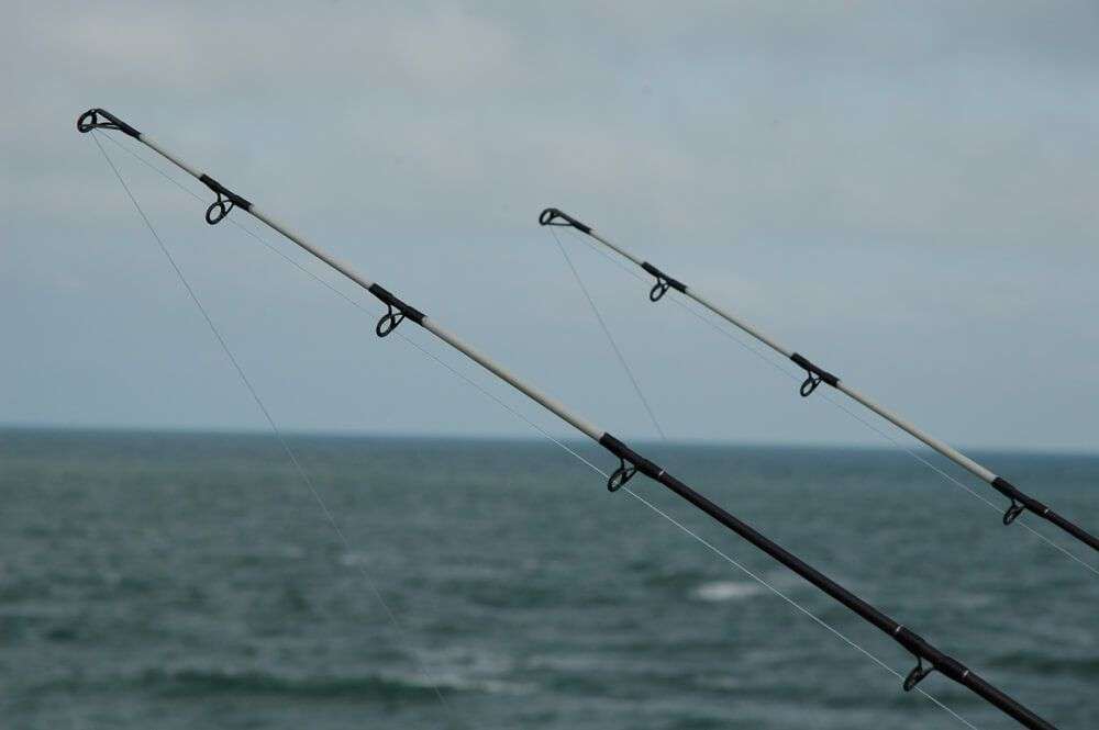 Two fishing rod tips pointed towards a vast, cloudy ocean horizon.