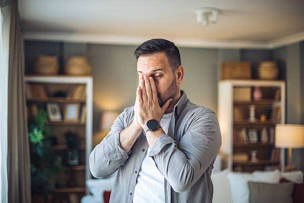 Worried man covering his face with his hands, standing in his living room